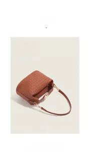 Detail of caramel woven leather texture with gold metal lock on minimalist shoulder bag