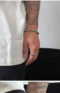 Detail of a men's silver chunky chain bracelet and ring worn on tattooed arm