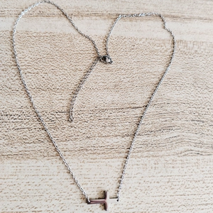 Detailed close-up of a silver stainless steel cross pendant on a thin link chain over wood