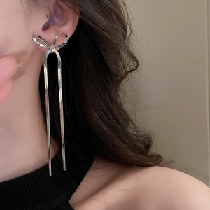 Detailed view of silver bow-shaped long tassel earrings on a model showing metal shine