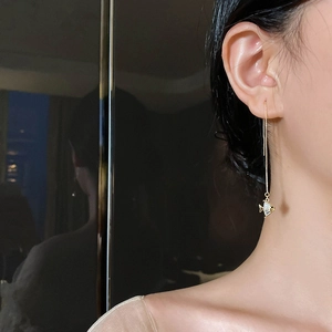 Gros plan sur de longues boucles d'oreilles dorées avec pendentif poisson en zircon brillant