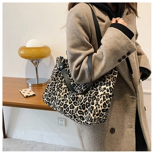 Detail of leopard print canvas tote bag featuring sturdy black leather straps on a model