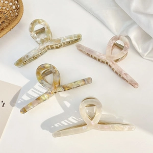 Detail of four marble patterned acetate claw clips in pastel colors on white silk fabric