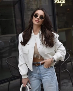 Close-up of white cropped jacket with oversized pockets and gold logo belt detail