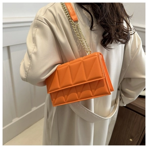 Chic orange quilted crossbody bag with gold chain strap worn with a beige trench coat
