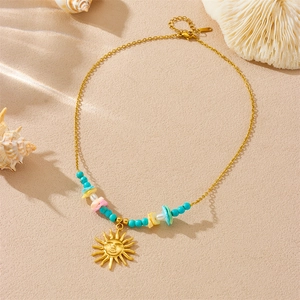 Gold sun pendant necklace with turquoise beads and shell accents on sand background