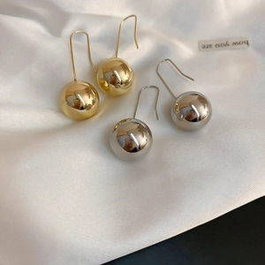 Flat lay of minimalist gold and silver metal ball drop earrings on white silk fabric