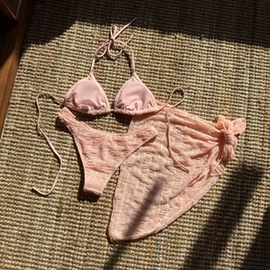Detail view of light pink three-piece bikini set with textured mesh fabric and sarong skirt