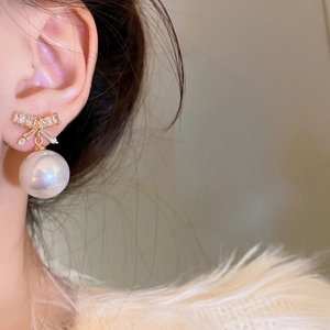 Close-up of elegant bow earrings with pearls and zircons worn by a female model
