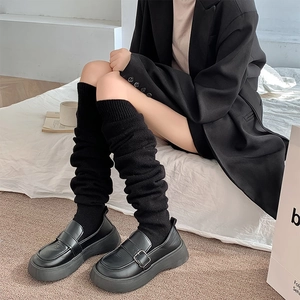 Detail of black ribbed knit over-knee socks paired with platform loafers and metal buckle