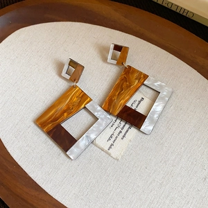 Detail of 18k gold-plated tiger eye earrings with brown marble texture on wood tray