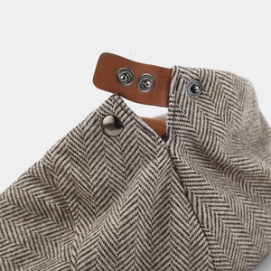 Detail of grey herringbone fabric and brown leather adjustable strap with metal snaps