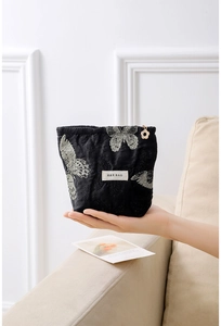 Close-up of black jacquard pouch with silver butterfly embroidery and floral gold zipper