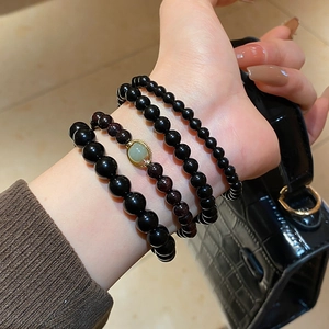 Close-up of stacked obsidian beads, garnet stones, and green jade pendant on female wrist