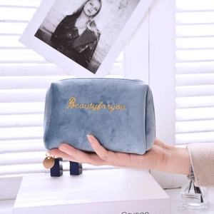 Blue velvet makeup bag with gold embroidery and zipper closure shown in hand