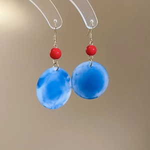 Détail de boucles d'oreilles vintage en acrylique avec perles rouges et disques bleus marbrés