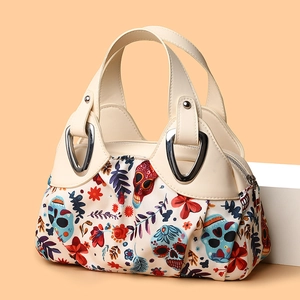 Women handbag with floral skull pattern and cream leather handles on orange background