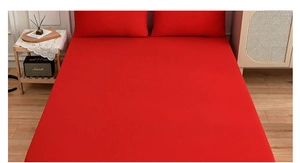 Detail view of solid red bedding set including fitted sheet and two pillowcases on floor
