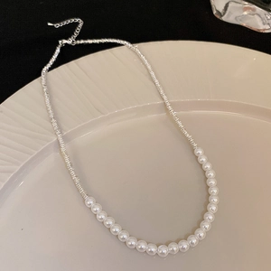 Detail of a chic split design necklace featuring silver chain and white pearls on a tray