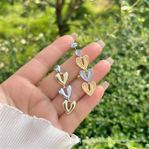 Détail de boucles d'oreilles pendantes à trois cœurs liés en or et argent bicolores