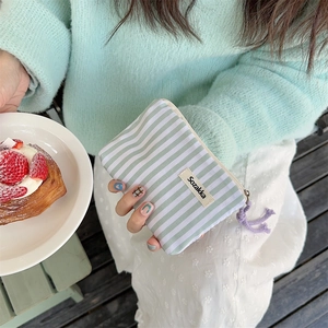 Close-up of mint green striped canvas pouch with a purple tassel and brand label