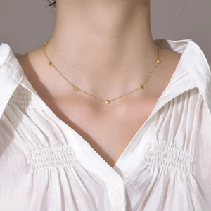 Close-up of five dainty gold heart pendants on a titanium steel necklace worn by a model