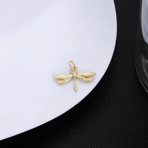 Detailed view of a golden 18K plated dragonfly pendant with intricate mesh wing texture