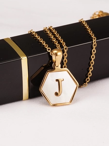 Vista macro del colgante hexagonal de oro de 18K con nácar blanco y detalle de letra J