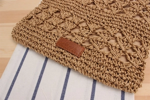 Close-up of brown woven straw bag texture with blank leather patch on striped fabric