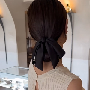 Large black satin bow hair clip on low bun hairstyle worn by a model in a minimal setting
