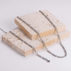 Polished silver Figaro chain necklace and bracelet on beige stone platform