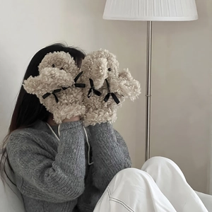 Détail de moufles en peluche beige avec nœuds noirs et texture douce en polaire