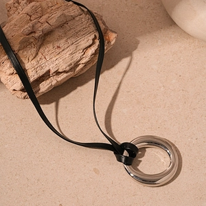Dettaglio di un ciondolo circolare in metallo argento con cordino in pelle nera regolabile