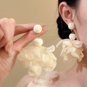 Close-up of elegant off-white chiffon flower earrings featuring textured raffia beads.