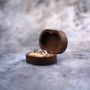 Oval walnut wood ring box with burlap interior holding two rings on grey background