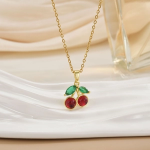 Elegant gold cherry pendant necklace with red crystals and green leaves on silk background
