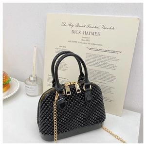 Detail of black PVC shell bag with studded texture and golden chain strap on desk