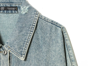 Detailed close-up of light blue denim jacket collar with textured stitching and size tag
