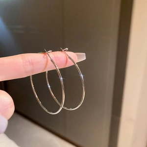 Gros plan de boucles d'oreilles créoles argentées tenues à la main au fini poli lisse