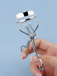 Close-up of ergonomic stainless steel eyelash curler with silicone pad on blue background