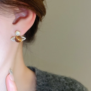 Detail of planet-shaped earring with brown stone, cross top, and crystals on model