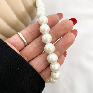 Detail of white faux pearl chain strap on a chic crossbody bag with hand close-up