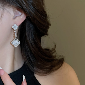 Detail of silver-tone clover drop earrings with white zircon on female model