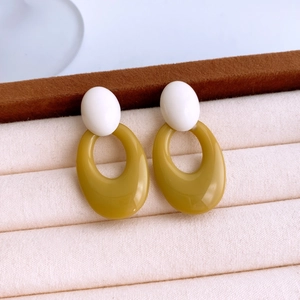 Macro shot of stylish white and mustard yellow acrylic hollow oval earrings on beige tray