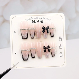 Macro shot of French tip press-on nails with glitter, black bows, and rhinestones on cards