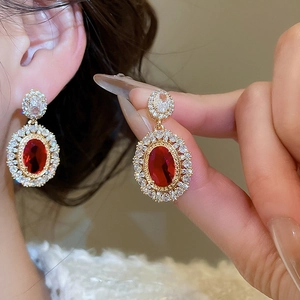 Detail of elegant gold-plated oval red gemstone earrings with white zircon accents