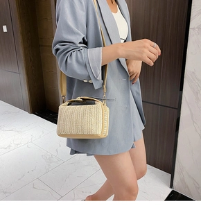 Detail of straw crossbody bag with leather trim on model in a soft indoor setting