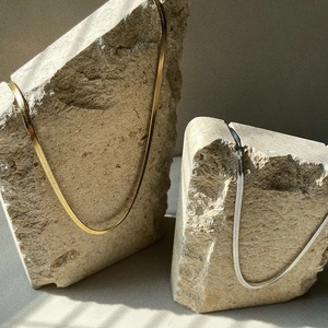 Flat snake bone necklaces in gold and silver colors resting on light natural stones
