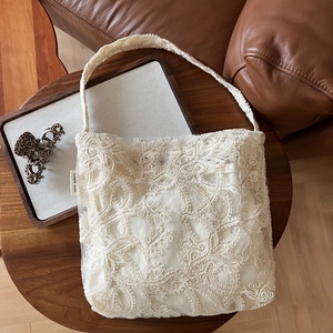 Detailed shot of white floral lace tote bag on a wooden table with elegant accessories