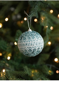 Close-up of a teal glitter Christmas ball with white lace hanging on a festive tree